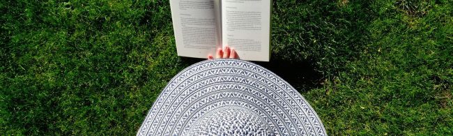 Frau mit Hut liest Buch im Gras. Perfekt für gesunde Ernährung und Fitness.