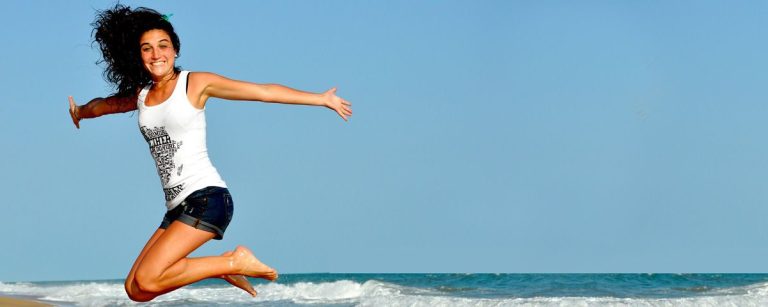 Frau springt vor Freude am Strand, inspiriert von gesunder Ernährung und Fitness.