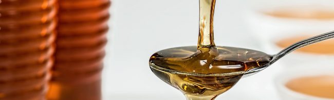 Sirup auf einem Löffel, vor einem unscharfen Hintergrund, der eine Ernährung für Fitnesskunden symbolisiert.