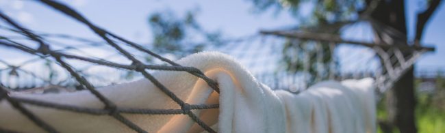 Weißes, flauschiges Handtuch in einer Hängematte, im Hintergrund verschwommene Bäume und blauer Himmel – ideal für Sportler.