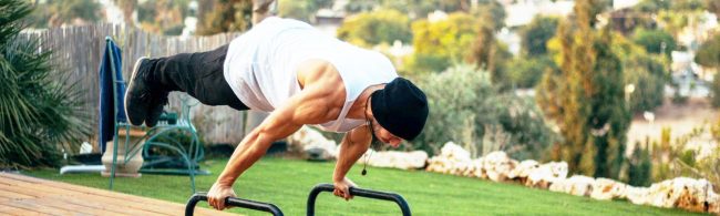 Mann macht Handstand-Liegestütze auf Parallettes im Freien.