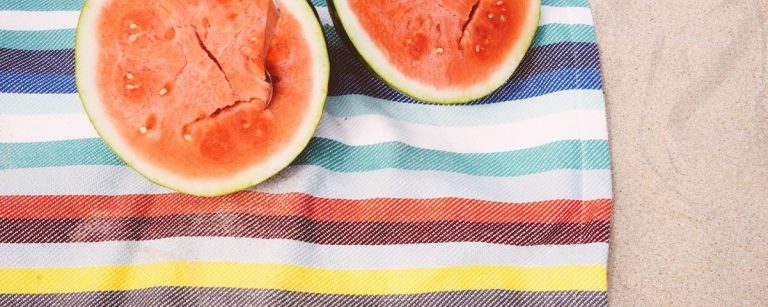 Zwei Wassermelonen auf einem gestreiften Handtuch am Strand – perfekt für eine gesunde Fitness-Ernährung.