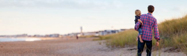 Vater trägt Sohn am Strand, gesunde Ernährung für Familien.