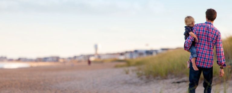 Vater trägt Sohn am Strand, gesunde Ernährung für Familien.