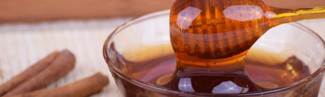 Goldener Honig fließt von einem Löffel in eine Schüssel, daneben Zimtstangen – perfekt für Fitness-Rezepte.