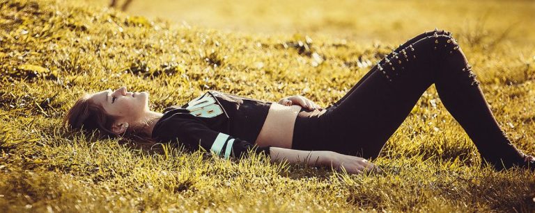 Junge Frau liegt auf sonnenbeschienener Wiese und entspannt sich, perfekt für Fitness und Ernährung.