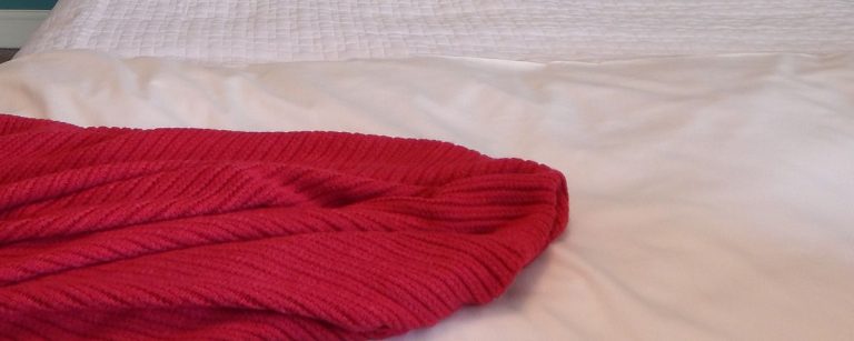 Rote Strickdecke auf einem weißen Bett, ideal für ein gemütliches Zuhause nach dem Training.