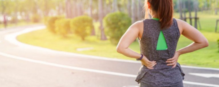 Frau mit Rückenschmerzen beim Laufen im Park. Ernährung für Sportler.