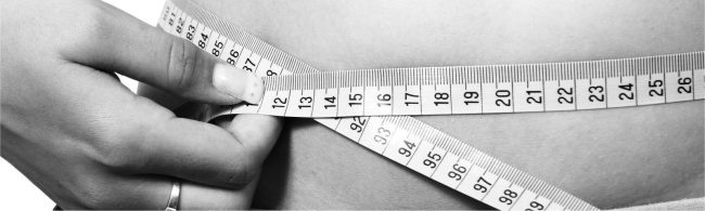 Eine Hand misst die Taille mit einem Maßband, was Gewichtsverlust und Fitnessziele symbolisiert.
