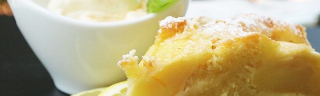 Ein Stück Zitronenkuchen bestäubt mit Puderzucker, serviert mit Eis und einer Zitronenscheibe.