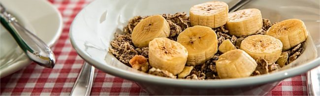 Müsli mit Bananenscheiben und einem Löffel auf karierter Tischdecke, perfekt für Fitness und gesunde Ernährung.