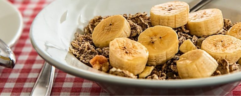 Müsli mit Bananenscheiben und einem Löffel auf karierter Tischdecke, perfekt für Fitness und gesunde Ernährung.