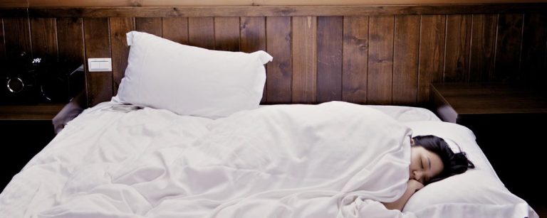 Eine Frau schläft im Bett, was auf eine gesunde Erholung für Fitness und Ernährung hinweist.