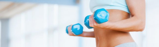 Frau mit Hanteln im Fitnessstudio trainiert, um fit und gesund zu bleiben.