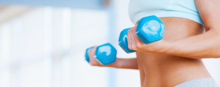 Frau mit Hanteln im Fitnessstudio trainiert, um fit und gesund zu bleiben.