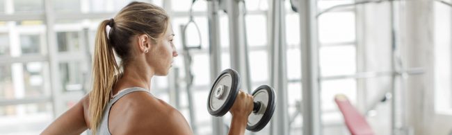 Frau mit Zopf trainiert mit Hantel im Fitnessstudio, inspiriert von gesunder Ernährung.