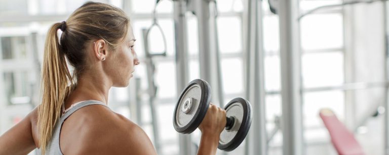 Frau mit Zopf trainiert mit Hantel im Fitnessstudio, inspiriert von gesunder Ernährung.