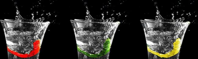 Gesunde Getränke mit Fruchtstücken: rote Beere, grüner Apfel und gelbe Zitrone in Wasserspritzern.