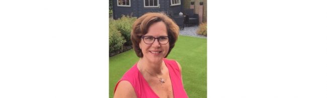 Frau mit Brille und pinkfarbenem Oberteil, lächelnd im Garten – ideal für Fitness- und Ernährungsblogs.