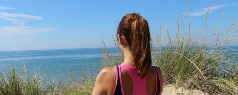 Frau mit Pferdeschwanz blickt aufs Meer, trainiert für gesunde Ernährung.