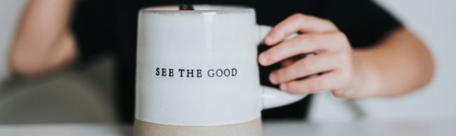 "Sehen Sie das Gute" auf einer Tasse, die von einer Hand gehalten wird – ein Symbol für Wohlbefinden und gesunde Ernährung.