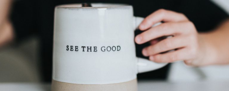 "Sehen Sie das Gute" auf einer Tasse, die von einer Hand gehalten wird – ein Symbol für Wohlbefinden und gesunde Ernährung.