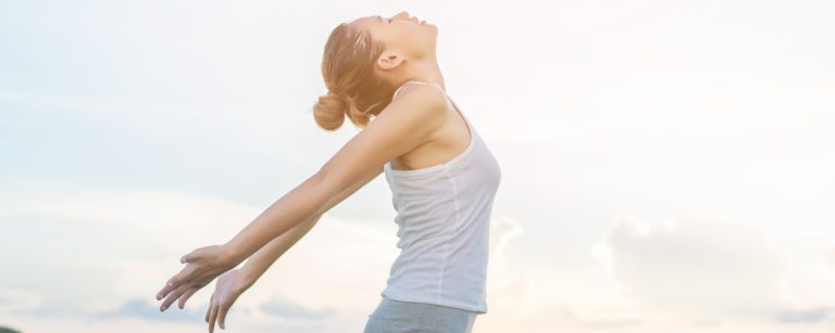 Frau mit ausgebreiteten Armen atmet tief durch und genießt die frische Luft.