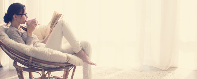 Frau im Sessel liest und trinkt, entspannt und ernährt sich gesund.