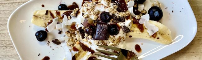 Fitness-Dessert: Banane mit Joghurt, Granola, Beeren, Kokoschips und Schokolade.