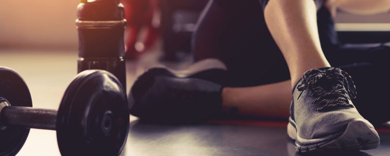 Dumbbells, Wasserflasche und Beine im Fitnessstudio, bereit für ein Training, ideal für Fitness-Ernährungsunternehmen.