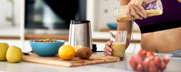 Frau macht Smoothie in der Küche, gesunde Ernährung für Fitness.