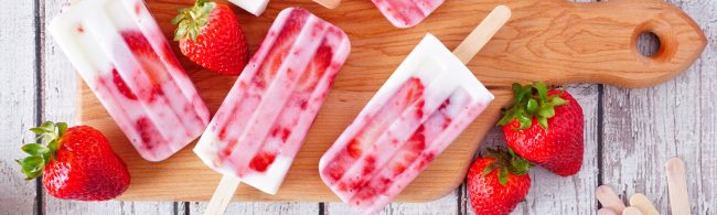 Vegane Erdbeer-Joghurt-Eisriegel auf Holzbrett mit frischen Erdbeeren.