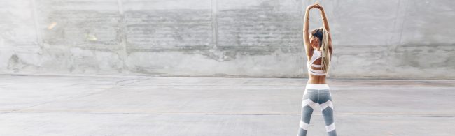 Sportlerin in weißem Sport-BH und grau-weißer Leggings streckt Arme über dem Kopf, Fitness und gesunde Ernährung.