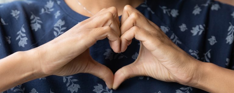 Hände formen Herz vor floralem Oberteil, Symbol für Herzgesundheit und Fitness.