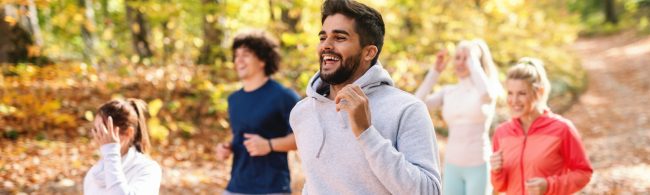 Lächelnde Menschen beim Joggen im Herbstwald, fit und gesund dank gesunder Ernährung.