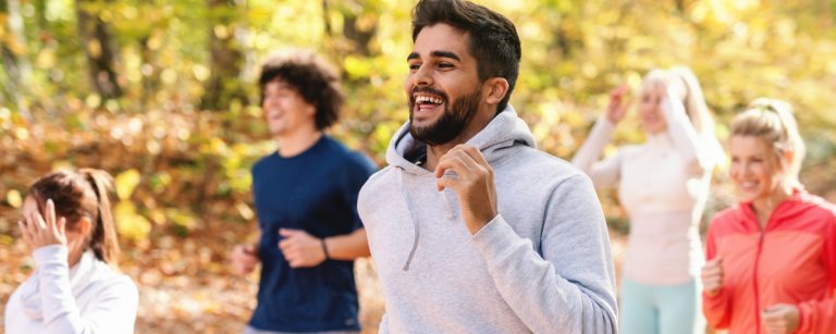 Lächelnde Menschen beim Joggen im Herbstwald, fit und gesund dank gesunder Ernährung.