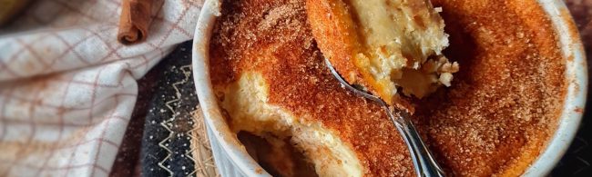 Slice of pear churro cheesecake with glossy caramelised pear wedges on top and a cinnamon-sugar crumb edge on a white plate.