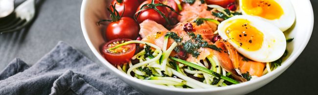 Zucchini noodle salad with smoked salmon, cherry tomatoes and arugula, drizzled with lemon-olive oil dressing on a light plate.