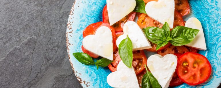 A plated three-course meal for Valentine’s Day featuring heart-shaped mozzarella Caprese salad, herbed grilled chicken with lemon, and chocolate-covered fruit treats.