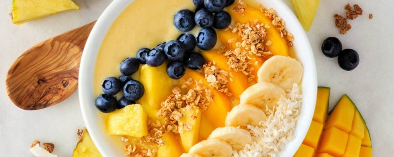 A vibrant tropical smoothie bowl topped with blueberries, pineapple chunks, pistachios, flaxseed, and coconut flakes.