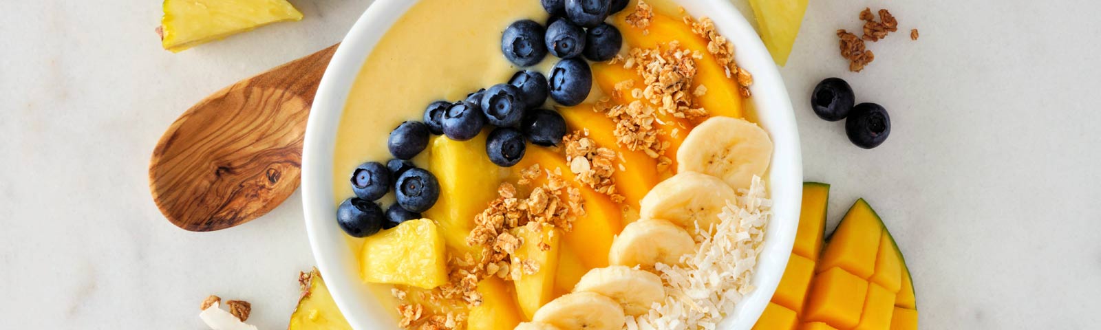 A vibrant tropical smoothie bowl topped with blueberries, pineapple chunks, pistachios, flaxseed, and coconut flakes.