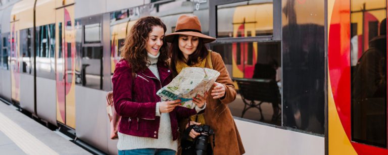 Zwei Frauen studieren mit einem Stadtplan eine Zugroute, ideal für Fitness-Reiseplanung.