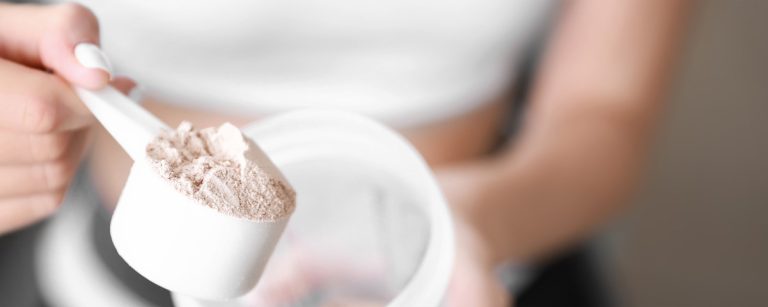 Nahaufnahme einer Frau, die BenFit Proteinpulver als Nahrungsergänzungsmittel mit einem Messlöffel aus einer Dose für ihre Fitness-Ernährung entnimmt.