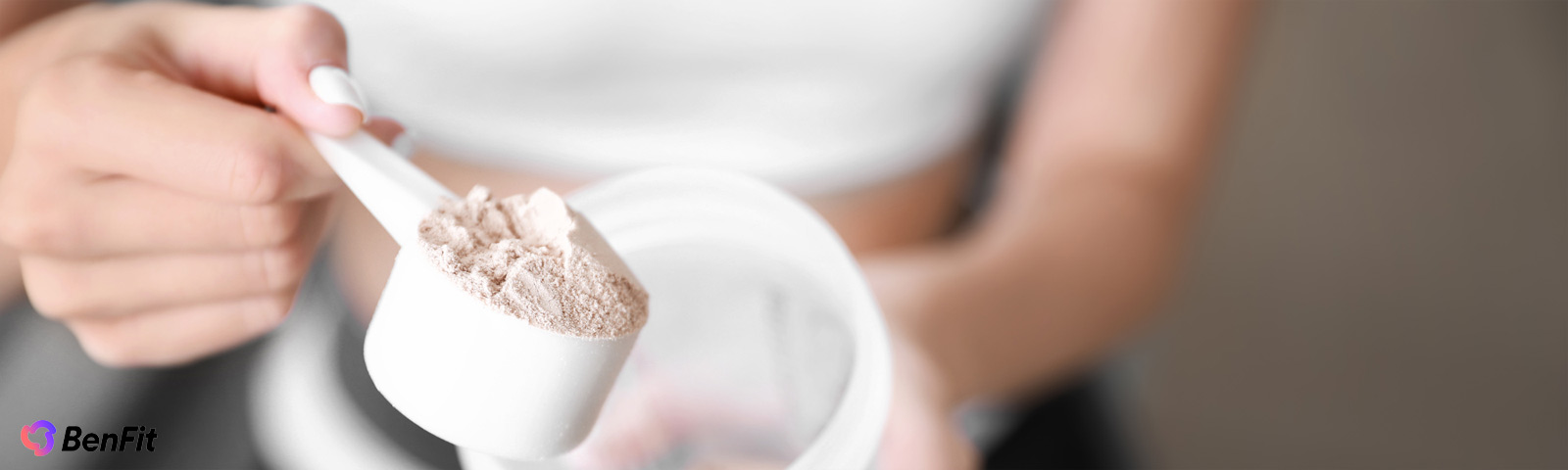 Nahaufnahme einer Frau, die BenFit Proteinpulver als Nahrungsergänzungsmittel mit einem Messlöffel aus einer Dose für ihre Fitness-Ernährung entnimmt.