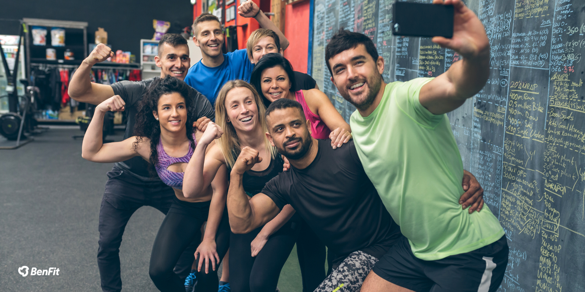 Nieuwsbrief juiste formaat (1) Gruppe von glücklichen Fitness-Enthusiasten posiert für ein Selfie im Fitnessstudio vor einer Tafel mit Trainingsübungen und Notizen.
