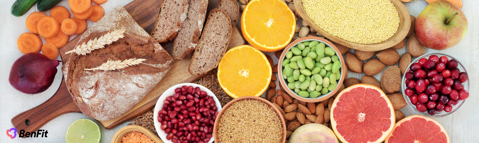 bf_hongerremmer BenFit: Vielfältige Auswahl an gesunden Lebensmitteln wie Vollkornbrot, frischem Obst (Orangen, Grapefruit, Apfel, Cranberries, Granatapfel), knackigem Gemüse (Karotten, Gurken, Zwiebel), Hülsenfrüchten (Linsen, Edamame), Vollkornprodukten (Hirse, Weizen) und Nüssen/Samen (Mandeln, Leinsamen). Ideal für eine ausgewogene, ballaststoffreiche und nährstoffreiche Fitness-Ernährung.